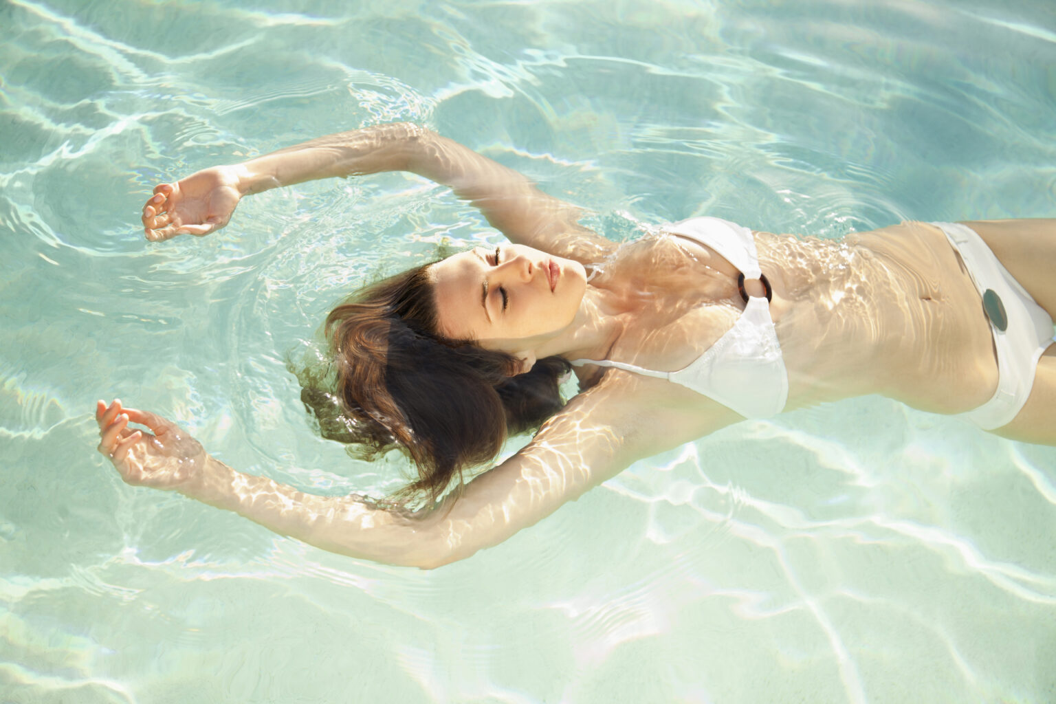 Floating ist eine Kunst der Entspannung. Das Bild zeigt eine Frau, die in kristallklarem Wasser schwebt, umgeben von sanften Wellen und schimmernden Sonnenstrahlen. Dies verkörpert das Gefühl von Schwerelosigkeit und innerem Frieden. Bei Wellness Wiesbaden können Sie diese tiefe Entspannung inmitten von Wiesbaden erleben.